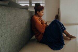 A woman with seasonal depression sits by her bed, holding her chest.